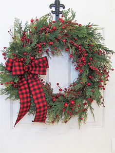 a christmas wreath with red berries and greenery hangs on a white door, next to a black cross