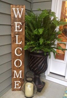 a wooden welcome sign next to a potted plant on the side of a house