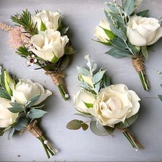 white roses and greenery are arranged on a gray surface with twine for garnish