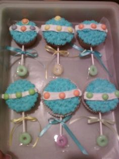 cupcakes decorated with blue frosting and bows are displayed in a box on the table