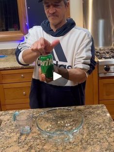 a man standing in front of a kitchen counter holding a cup and pointing to it