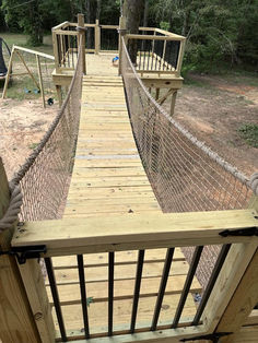 a wooden bridge that is in the middle of a forest with ropes hanging from it's sides