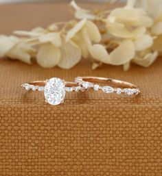 two engagement rings sitting next to each other on top of a brown cloth with flowers in the background