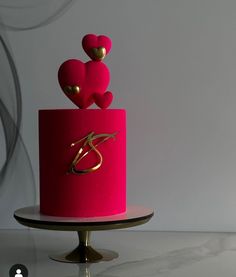 a pink cake with two hearts on top and gold decoration around the edges, sitting on a stand