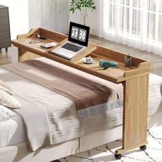 a laptop computer sitting on top of a wooden desk in front of a bed with white sheets