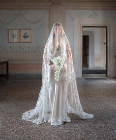 a woman in a wedding dress with a veil on her head and flowers in her hand