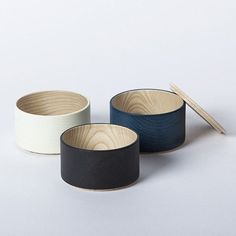 three wooden bowls with chopsticks in them on a white surface, one is black and the other is blue