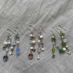 five pairs of dangling earrings with pearls and charms attached to them on a bed sheet