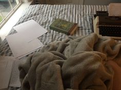 an unmade bed with books and papers on top of it next to a window