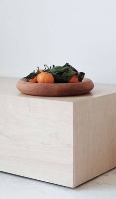 a wooden bowl filled with oranges on top of a white counter next to a plant