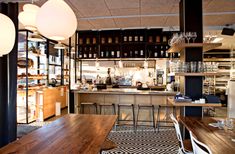 an empty restaurant with wooden tables and white lamps hanging from the ceiling, along with shelves full of wine bottles