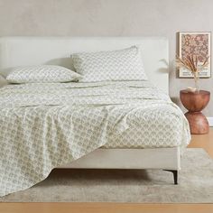 a bed with white sheets and pillows on top of it next to a brown vase