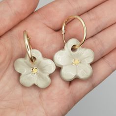 a pair of white flower shaped earrings on a person's hand with gold accents