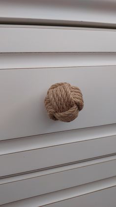 a rope is hanging on the side of a white cabinet with knoted handles and knobs