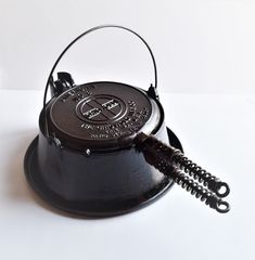 an old fashioned black tea kettle sitting on top of a white table with a cord attached to it