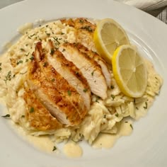 a white plate topped with chicken, pasta and lemon wedges