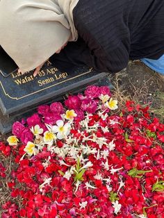 a person kneeling down next to a grave with flowers on it and a plaque in the background