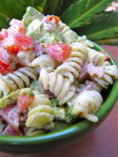 a green bowl filled with pasta salad on top of a table