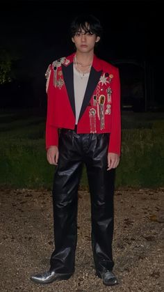 a young man in a red jacket and black pants standing on dirt ground at night