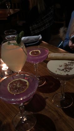 three different types of cocktails on a wooden table with people sitting at the bar