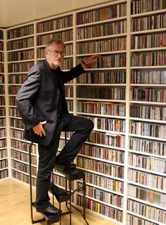 a man sitting on top of a chair in front of a book shelf filled with books