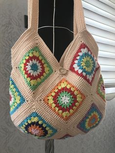 a crocheted bag hanging from a hook in front of a window with blinds