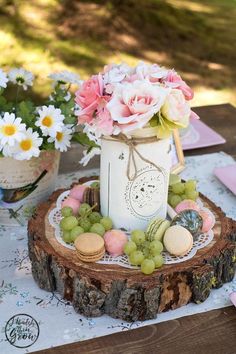 a table topped with a mason jar filled with flowers and grapes on top of a wooden slice