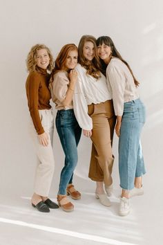 four women posing for the camera in front of a white wall with their arms around each other