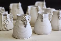 several white vases sitting on top of a table next to each other in different shapes and sizes