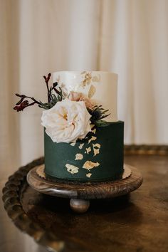 a green and white wedding cake with flowers on the top is sitting on a wooden stand