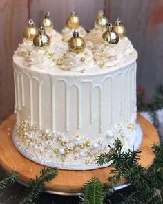 a white frosted cake with gold ornaments on top sitting on a wooden platter