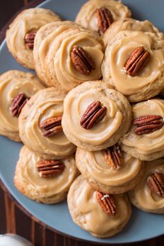 a blue plate topped with cookies covered in frosting and pecans on top of a wooden table