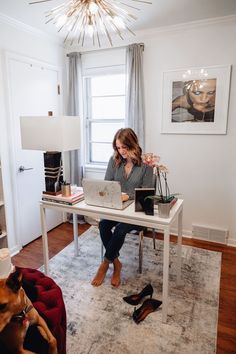 a woman sitting at a desk with her laptop on top of it, in front of a window