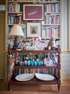 a book shelf filled with lots of books next to a lamp and pictures on the wall