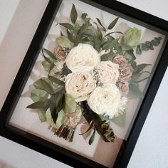 an arrangement of flowers is framed in a black frame on the wall next to a white wall