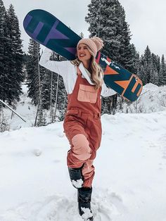 a woman carrying a snowboard on her back in the snow with trees in the background