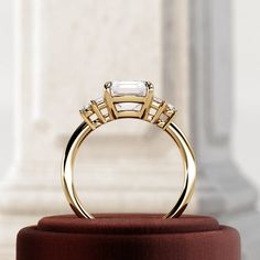 a three stone ring on top of a red velvet stand in front of a pillar