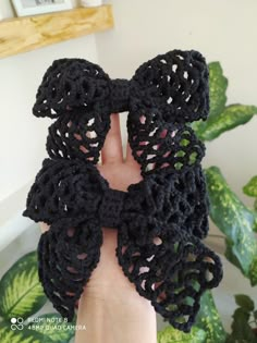 a hand holding up a black crocheted scarf with two large bows on it