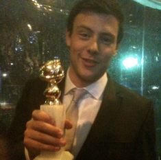 a man in a suit and tie holding up a golden award for best performance by an actor