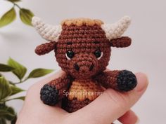 a small crocheted brown and white bull sitting on top of a person's hand