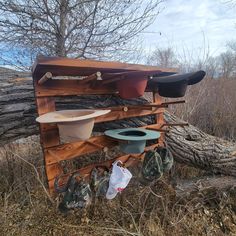 several hats and buckets are hanging on a wooden rack in the grass near a fallen tree