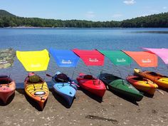 several kayaks are lined up on the shore with colorful umbrellas over their heads