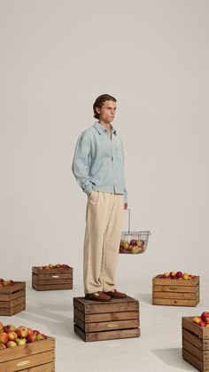 a man standing on top of wooden crates with apples in the background and one holding a basket