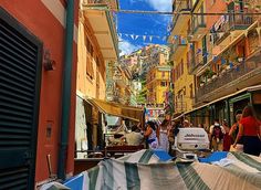 many people are walking down an alleyway with umbrellas on both sides and buildings in the background