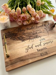 a wooden cutting board sitting on top of a table next to a candle and flowers