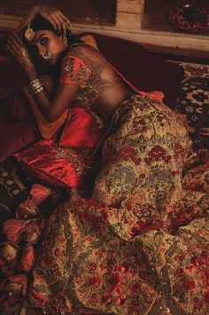 a woman sitting on top of a bed in a red and gold dress holding her hands to her face