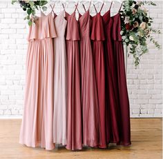 four bridesmaid dresses hanging up against a brick wall