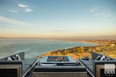 a living room with couches and a fire pit on top of a hill overlooking the ocean