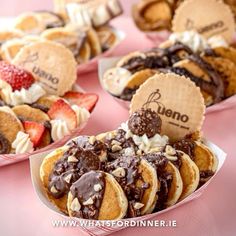 several desserts are arranged in pink trays with chocolate and strawberries on top