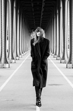 black and white photograph of a woman walking down an empty walkway with columns in the background